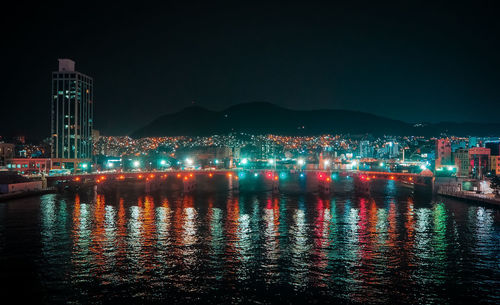 Illuminated buildings by sea against clear sky at night