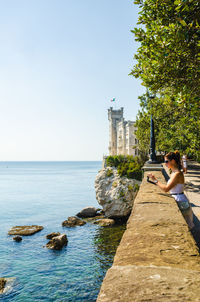 Man photographing on rock by sea against sky