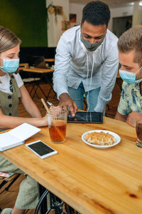 Cheerful friends wearing mask sitting at restaurant