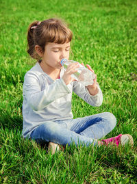 Young woman drinking water while sitting on grassy field
