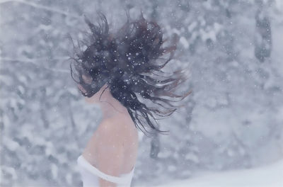 Side view of young woman walking in forest during snowfall