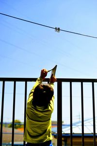 Rear view of child holding book standing by railing against sky