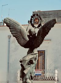 Low angle view of statue by building against sky