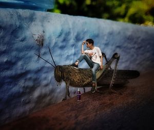 Young man sitting on umbrella against sky