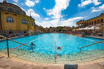 People swimming in pool against blue sky