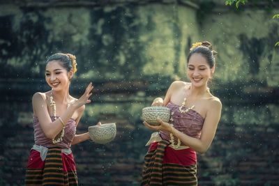 Happy young woman sprinkling water from bowl while standing against blurred background