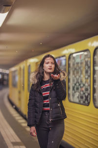 Thoughtful young woman holding confetti while standing against train at subway station