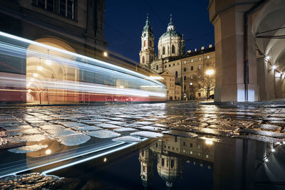 Light trail of tram in historic buildings. reflection in puddle on road. lesser town in prague.