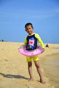 Full length of boy wearing inflatable ring on beach against sky