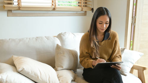 Portrait of young woman using digital tablet while sitting on sofa at home
