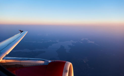 Airplane flying over lands against sky during sunset