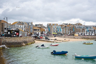 Boats moored on seaside by buildings in city against sky