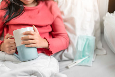 Midsection of woman holding coffee cup on bed