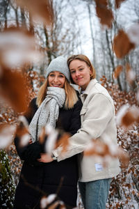 Portrait of smiling young womans standing against trees in winter forest
