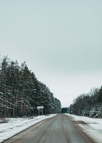 Road amidst trees against clear sky during winter