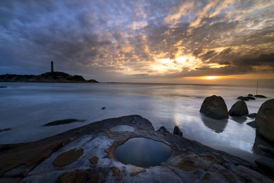 Scenic view of beach against cloudy sky during sunset