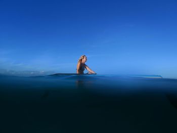 Side view of woman standing in sea against blue sky