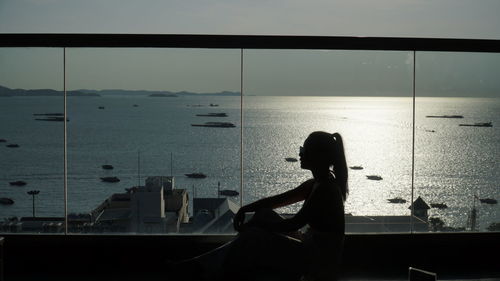 Silhouette woman looking at sea seen through window