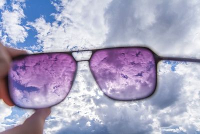 Close-up of hand holding sunglasses against blue sky