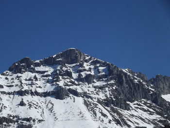 Low angle view of snowcapped mountains against clear blue sky