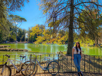Portrait of young woman standing by bicycle against trees