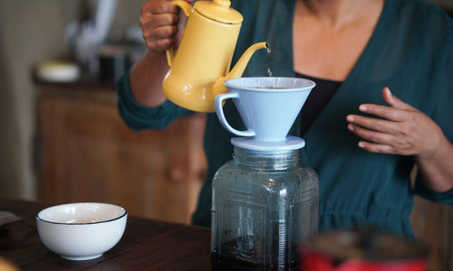 Midsection of woman pouring tea cup on table