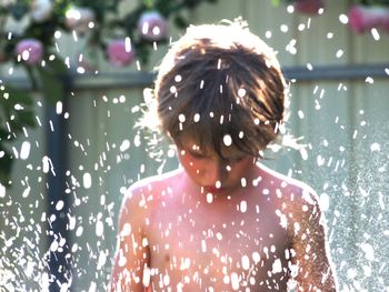 Close-up of shirtless boy in splashing water at yard