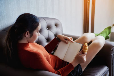 Woman having croissant with diary at home