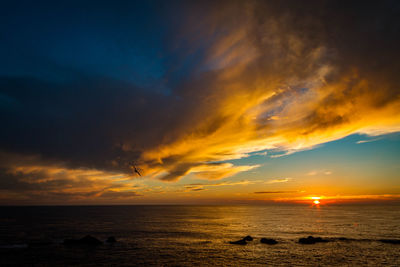 Scenic view of sea against dramatic sky during sunset