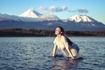 Young woman looking away while standing in lake against snowcapped mountain