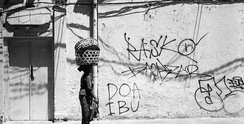 Woman with baskets on head walking against graffiti wall during sunny day