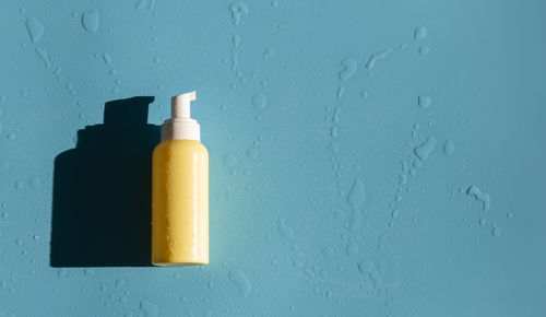 Yellow bottle with dispenser, and water drops on blue.