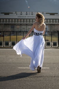 Full length of smiling woman holding dress while walking on road