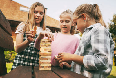 Three beautiful sisters are playing a wooden board game outdoors near their home.