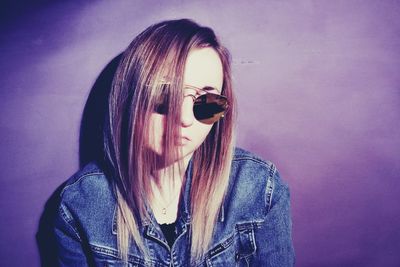 Portrait of young woman wearing sunglasses against wall