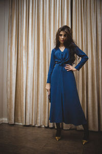 Portrait of a young woman standing against curtain