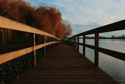 Footbridge by lake against sky