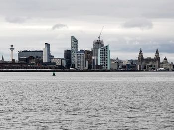 View of buildings by river against cloudy sky