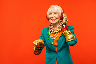 Smiling senior woman listening music against red background