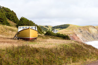 Low angle view of old yellow boat with pretty traditional houses perched on cliff , magdalen islands