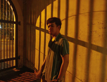 Portrait of young man standing by wall at night