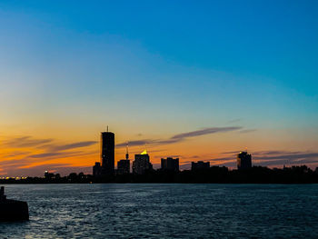 Silhouette buildings by sea against sky during sunset