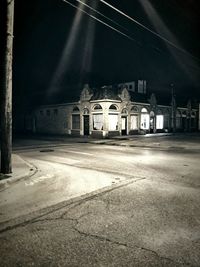 Empty road by illuminated buildings in city at night