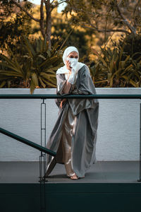 Full length picture of veiled woman with white niqab and hijab standing by railing