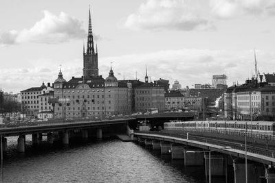 Bridge over river in city against cloudy sky