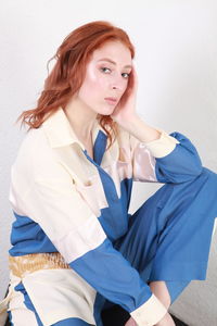 Portrait of young woman looking away while sitting against wall