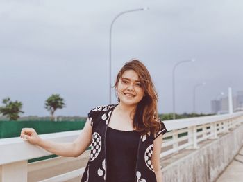 Portrait of smiling young woman standing against railing