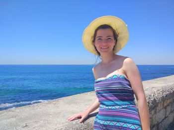 Portrait of smiling young woman wearing hat at beach against sky during sunny day