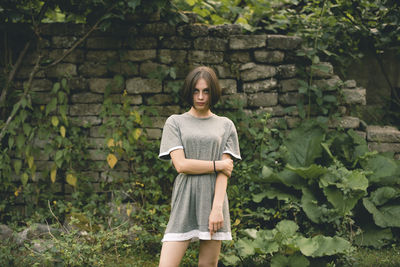 Portrait of a young woman standing against stone wall