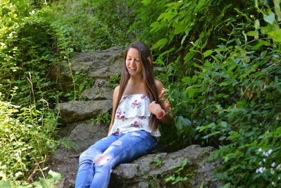 Young woman sitting on rock against plants